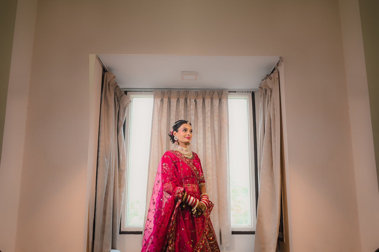 A beautiful Indian bride poses indoors wearing a vibrant traditional pink lehenga.
