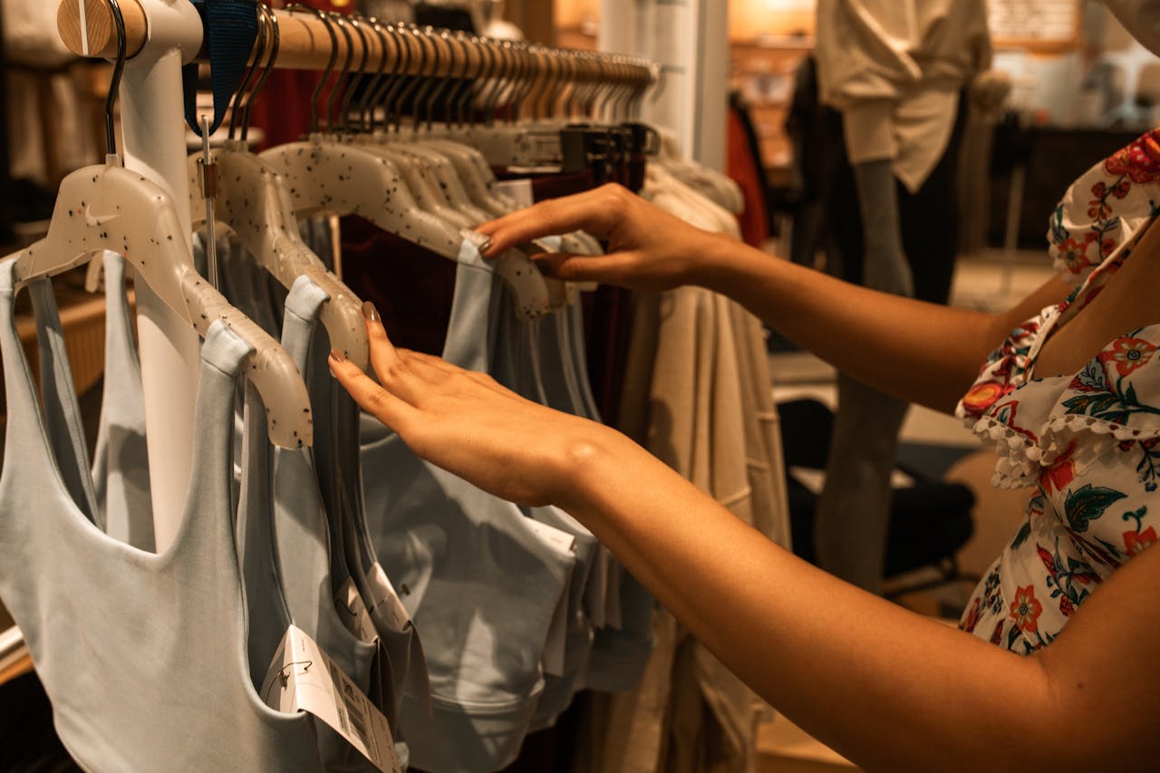 About A woman selecting blue tops from a clothing rack inside a fashion boutique.