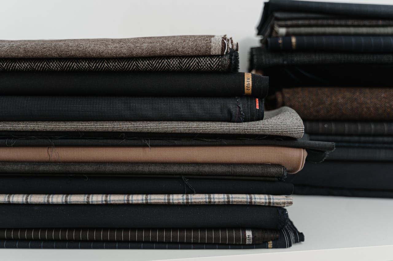 Services A neatly arranged pile of diverse fabrics, ideal for a fashion designer or tailor's workshop.