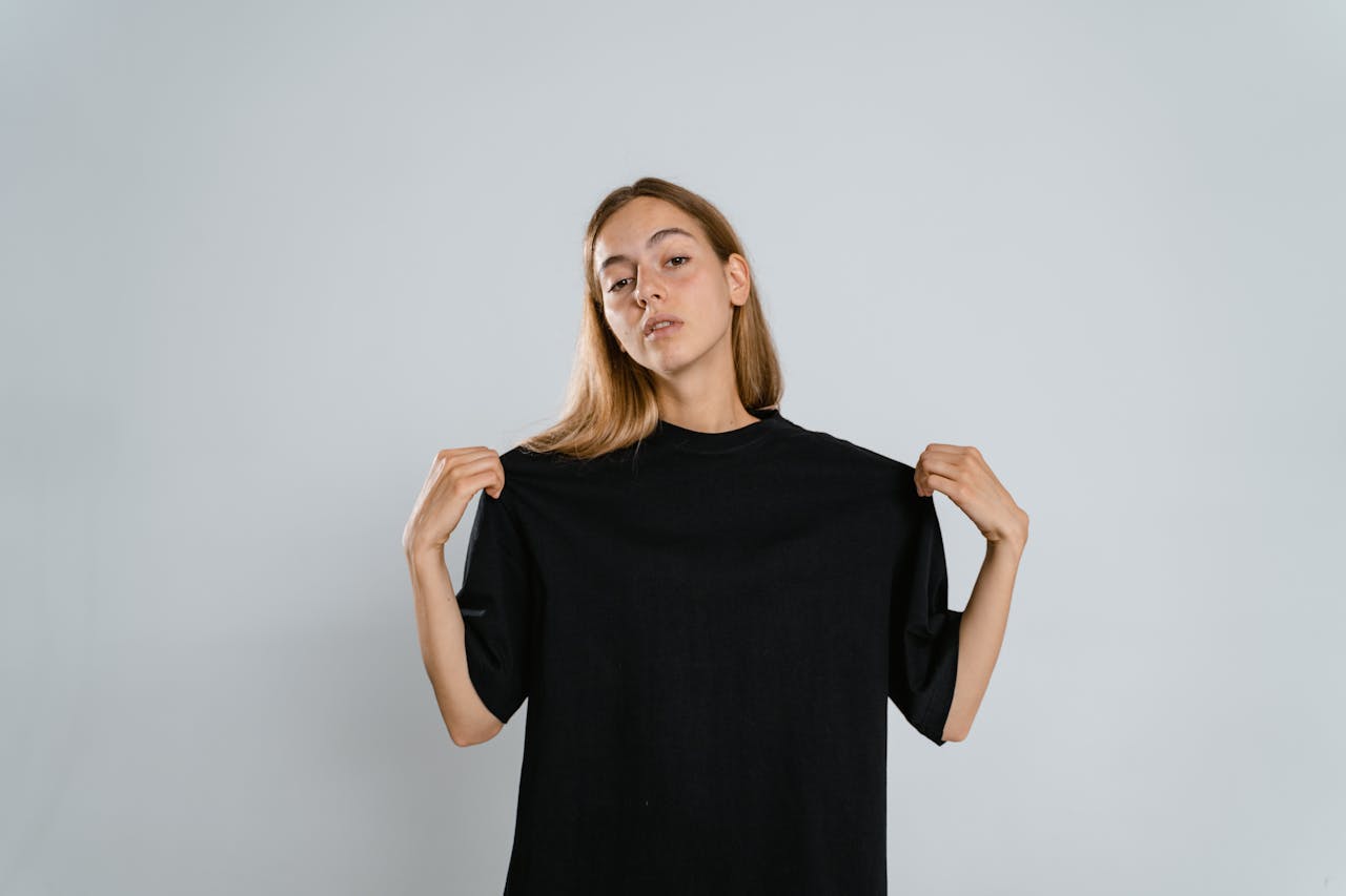 Services Teen girl in studio showing black T-shirt with arms raised against neutral background.